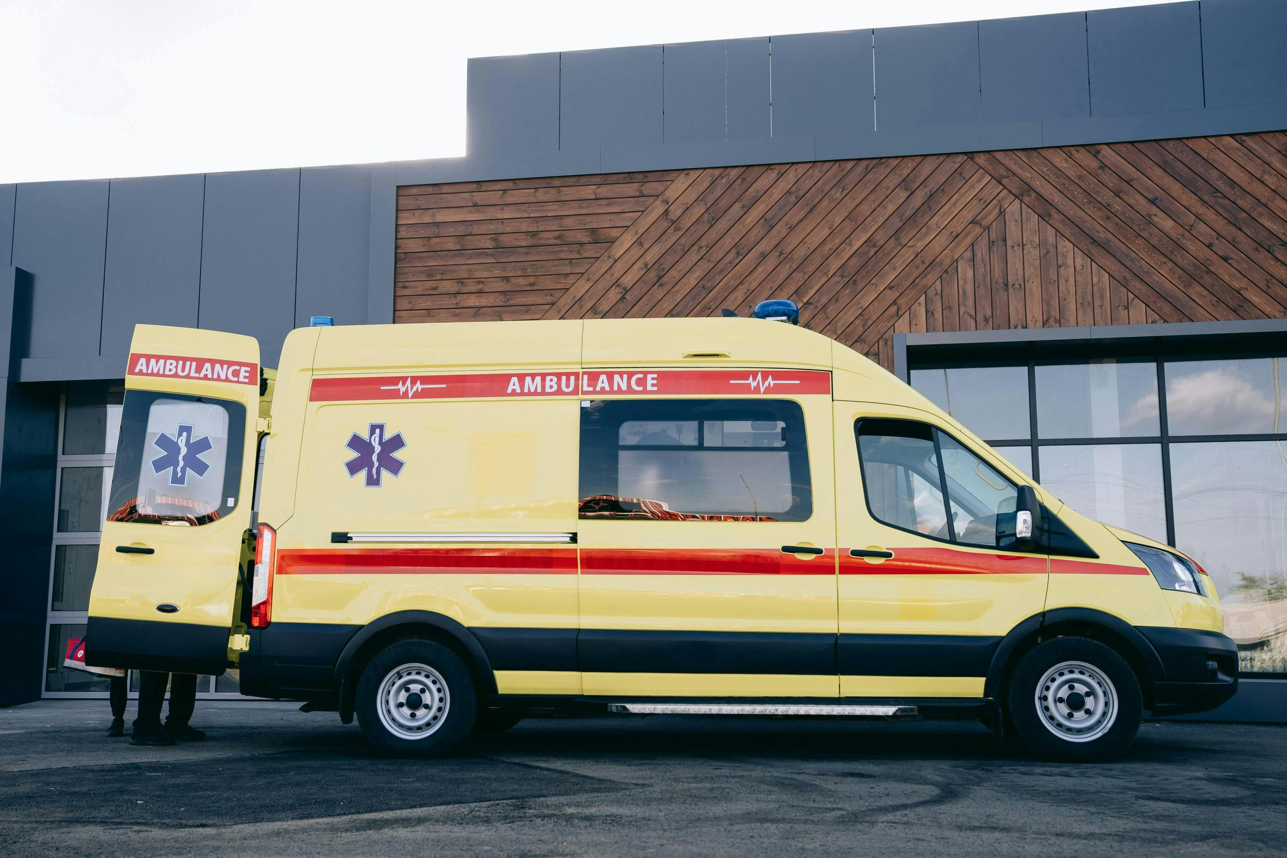 A yellow ambulance is parked outside a modern urban building. Emergency vehicle in city.